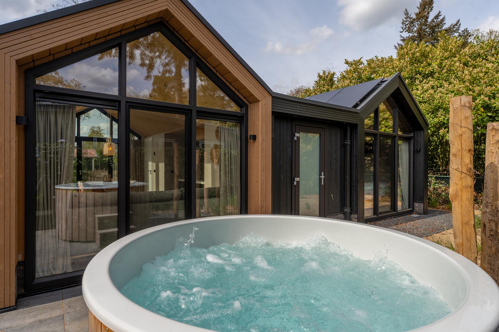 Eco Boslodge bij De IJsvogel met een bubbelende ronde jacuzzi voor de glazen gevel