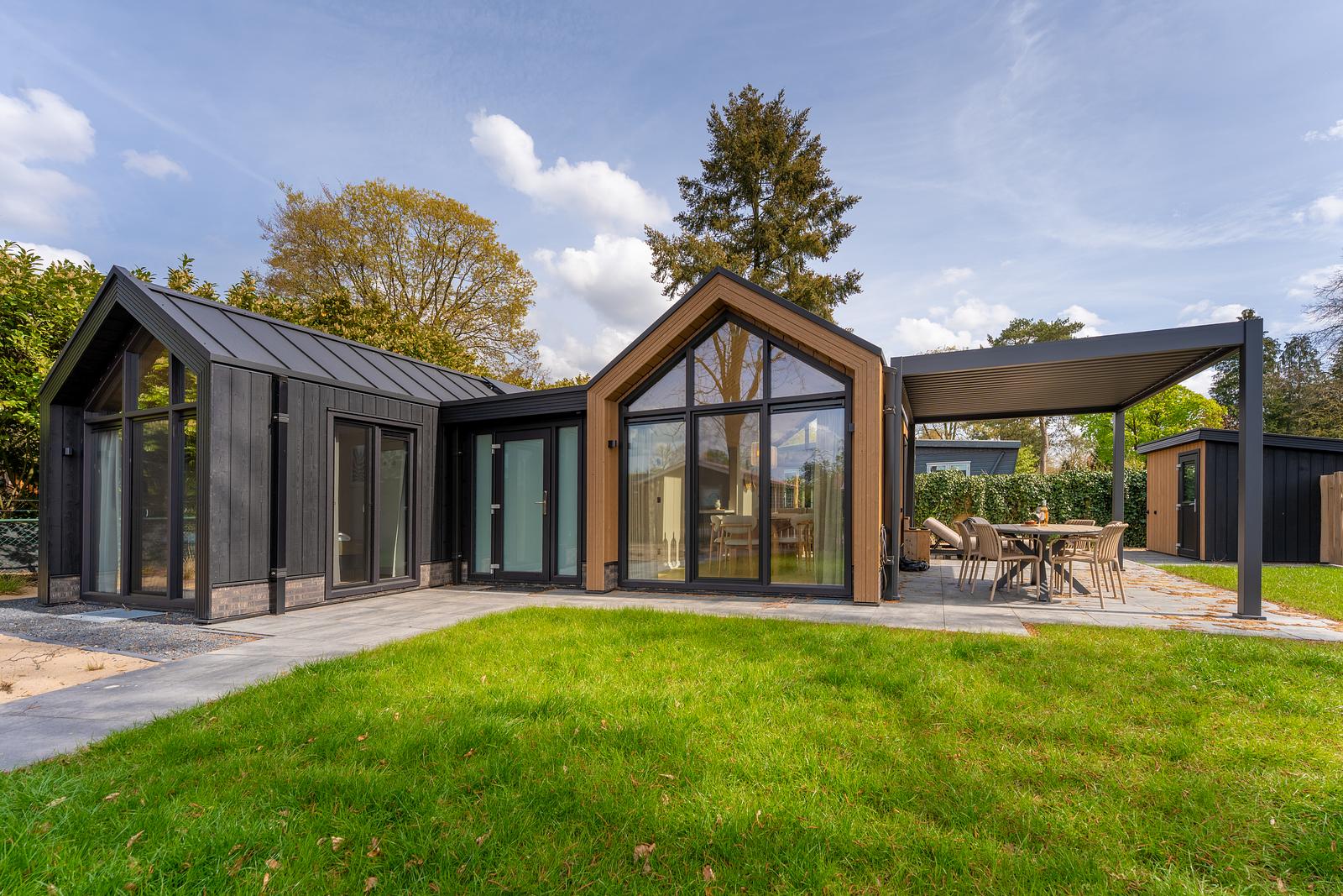 Eco Boslodge bij De IJsvogel met grote ramen, grasveld en eettafel onder een pergola