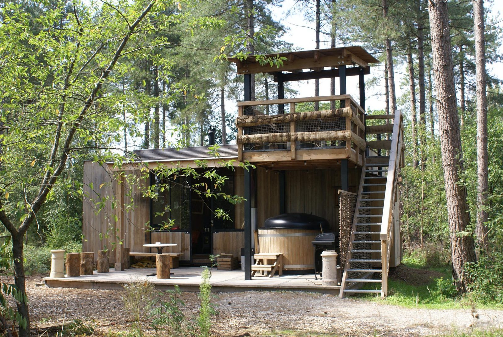 Treetrunk-cabin met overdekte hottub en buitentrap naar het hoge terras